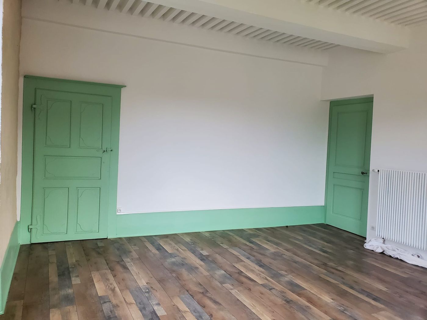 Chambre rénovée : murs blancs, boiseries vert d'eau et parquet flottant.