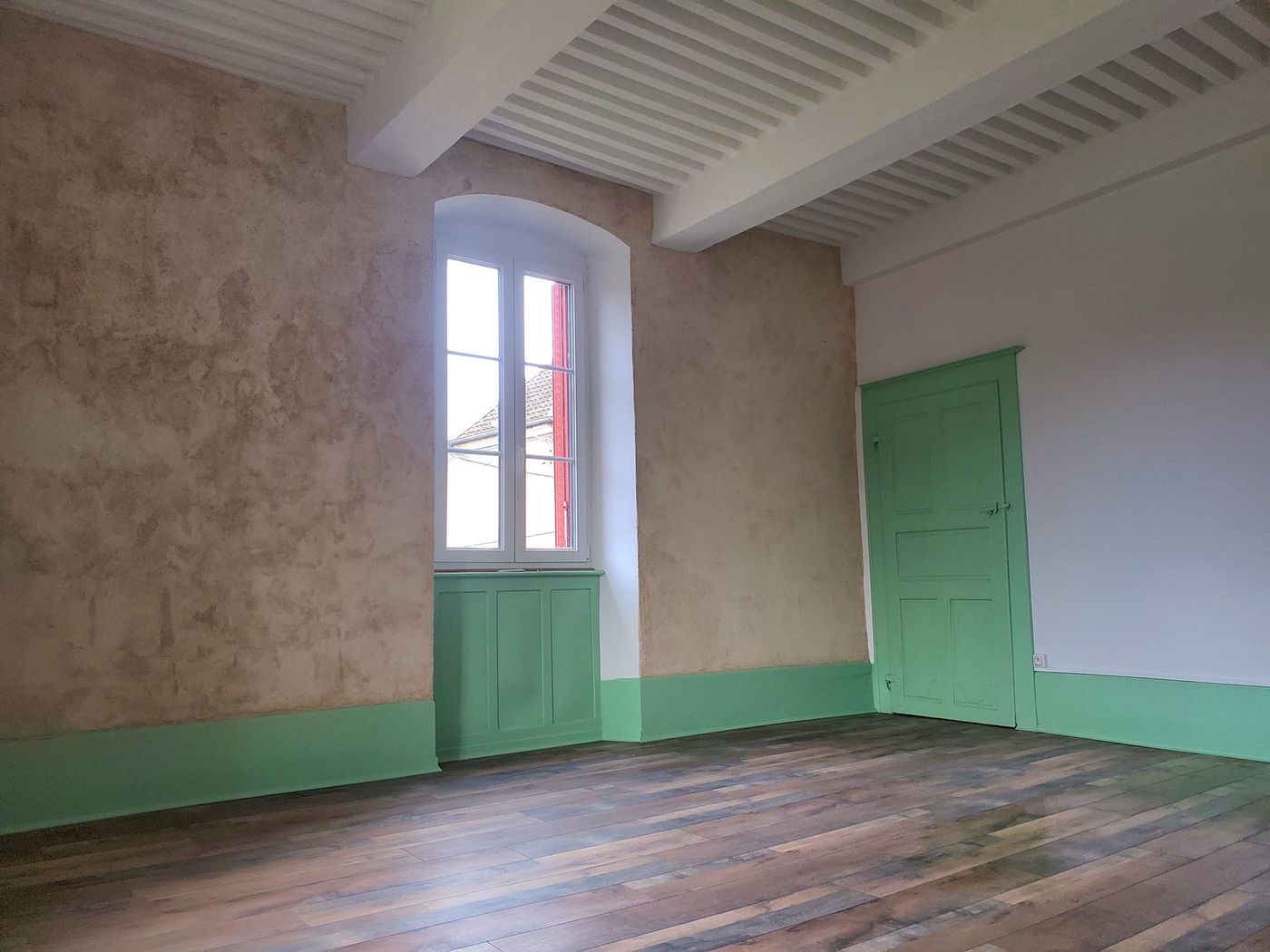 La chambre rénovée côté fenêtre, enduit décoratif et soubassement vert d'eau.