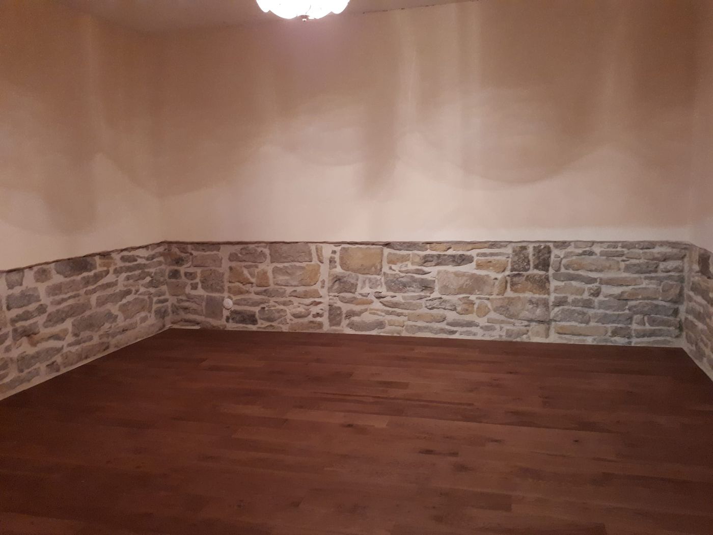 Salon rénové : pierres apparentes jointées à la chaux, enduit décoratif et parquet flottant.