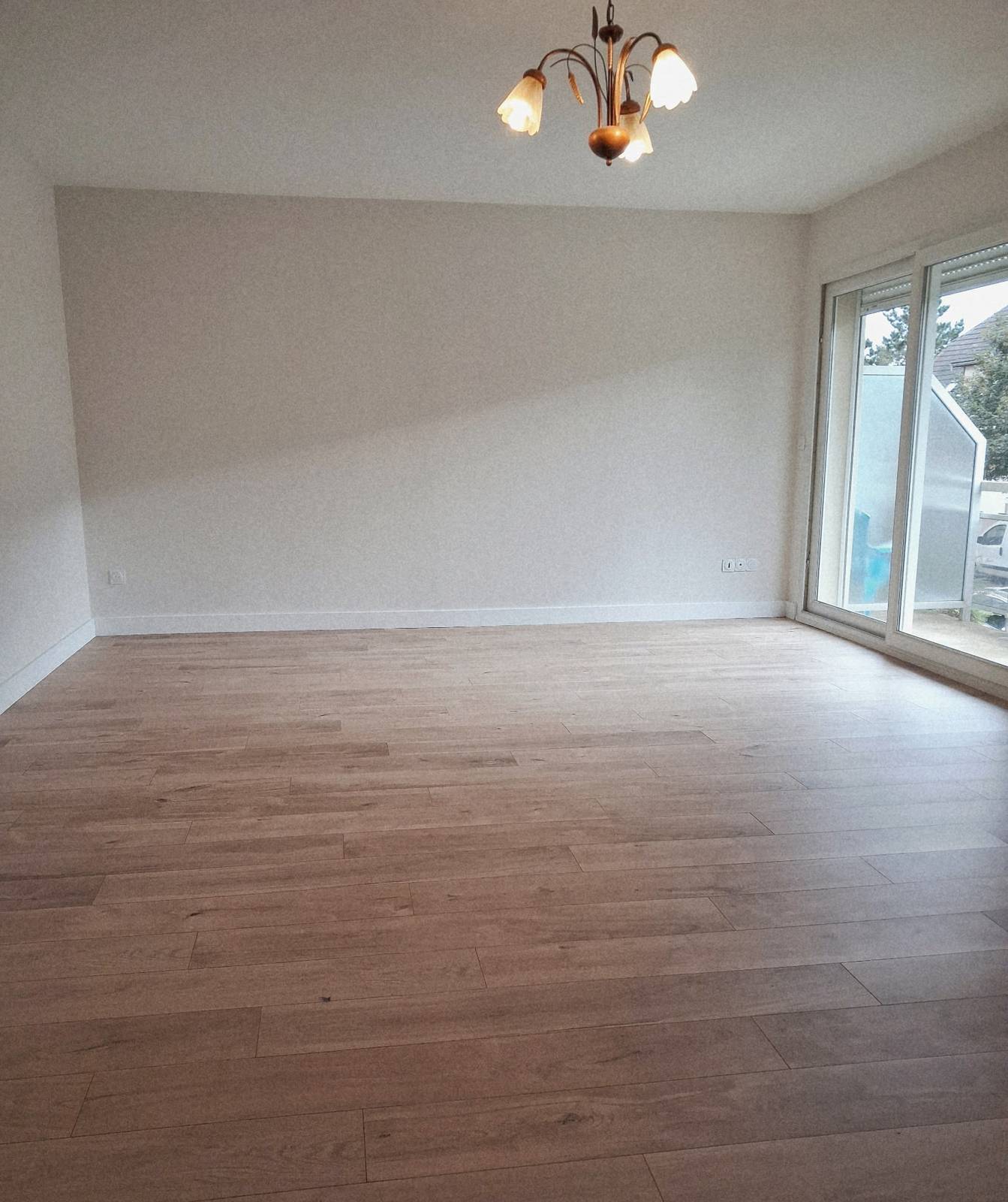 Le même salon après travaux : murs clairs, parquet flottant et plinthes blanches.