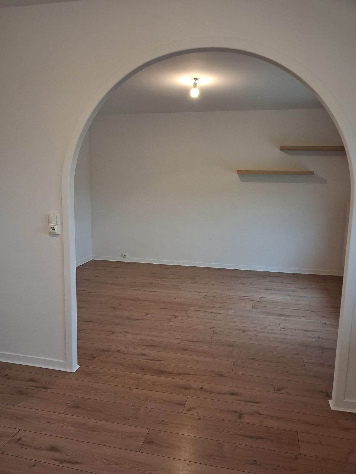 Passage en arche vers une pièce repeinte, le parquet flottant courant de part et d'autre.