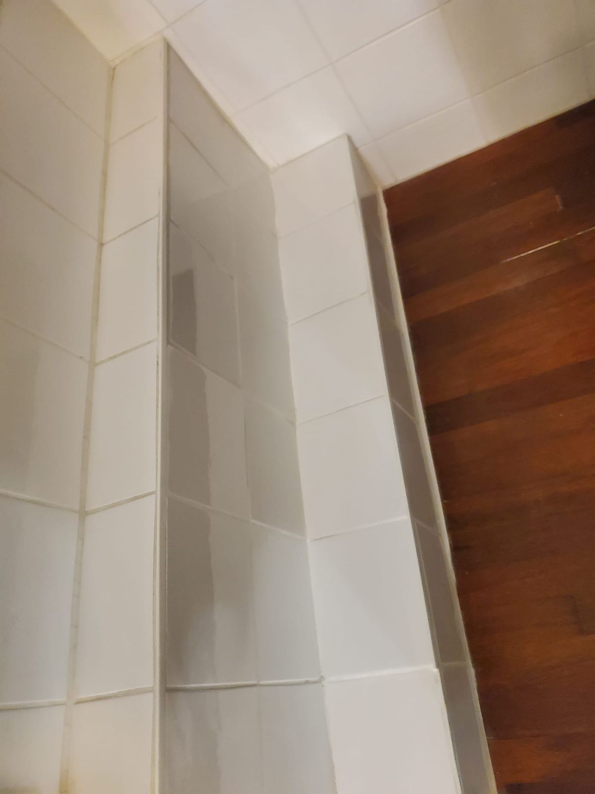 Angle de la salle de bain après travaux : faïence blanche et parquet exotique réparé.