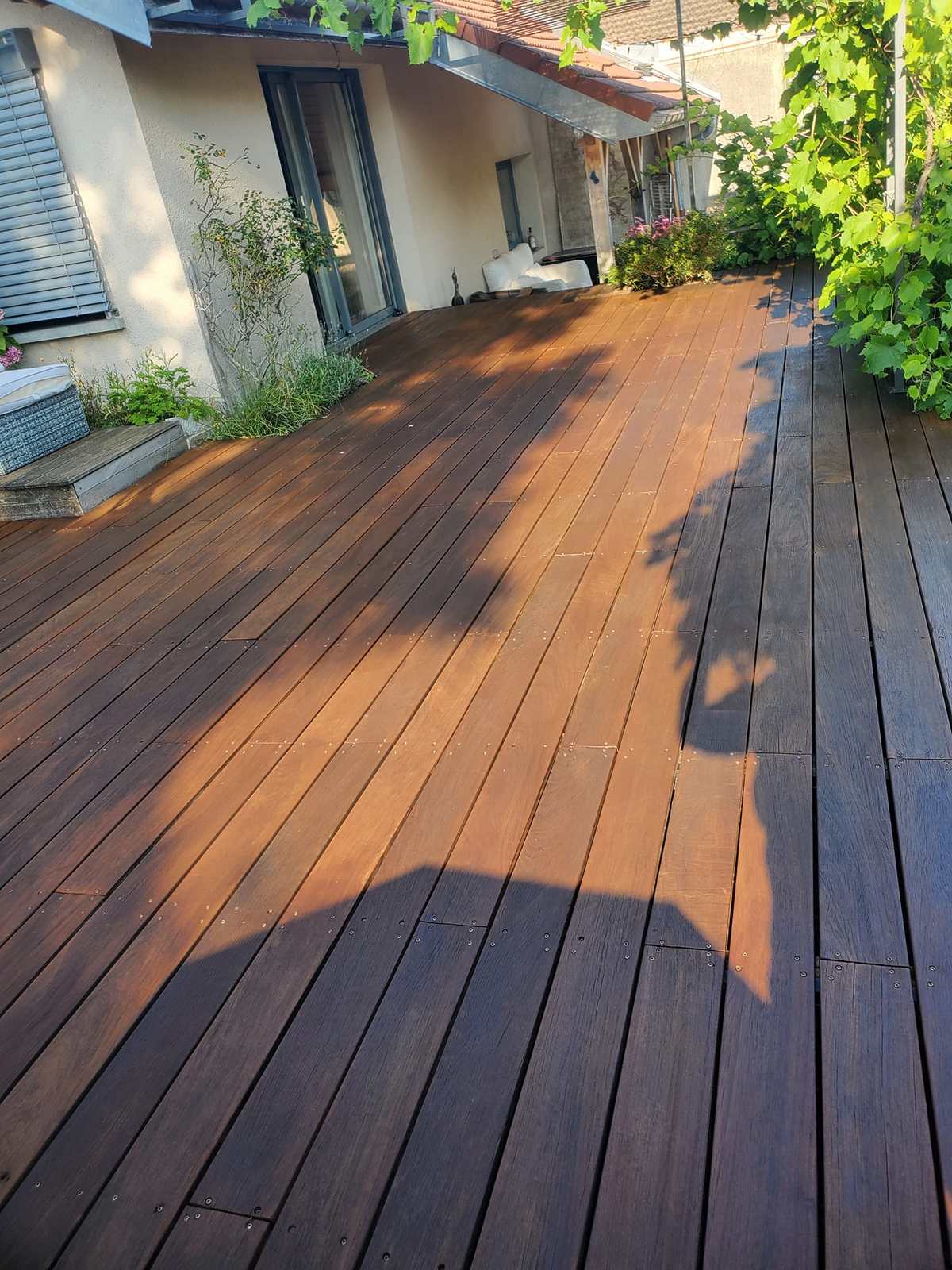 Terrasse en bois exotique dégrisée et huilée, sous les arbres.